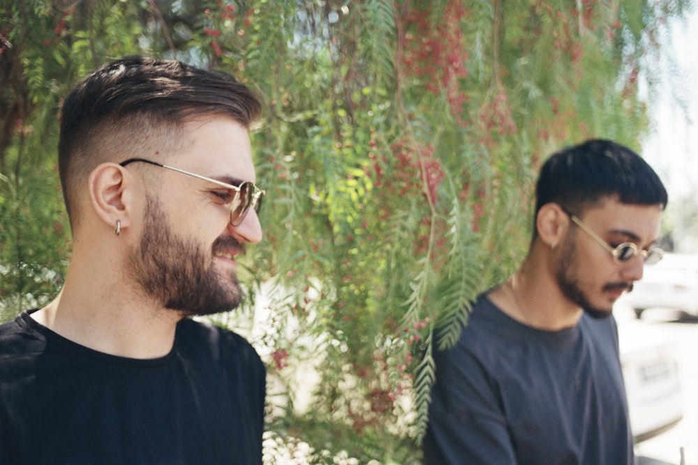 two men standing next to each other in front of a tree