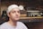 A man with a white bandana is sitting in front of a vintage radio and some kind of old equipment on shelves. The shelves have a rustic and industrial feel with wooden and metal elements.