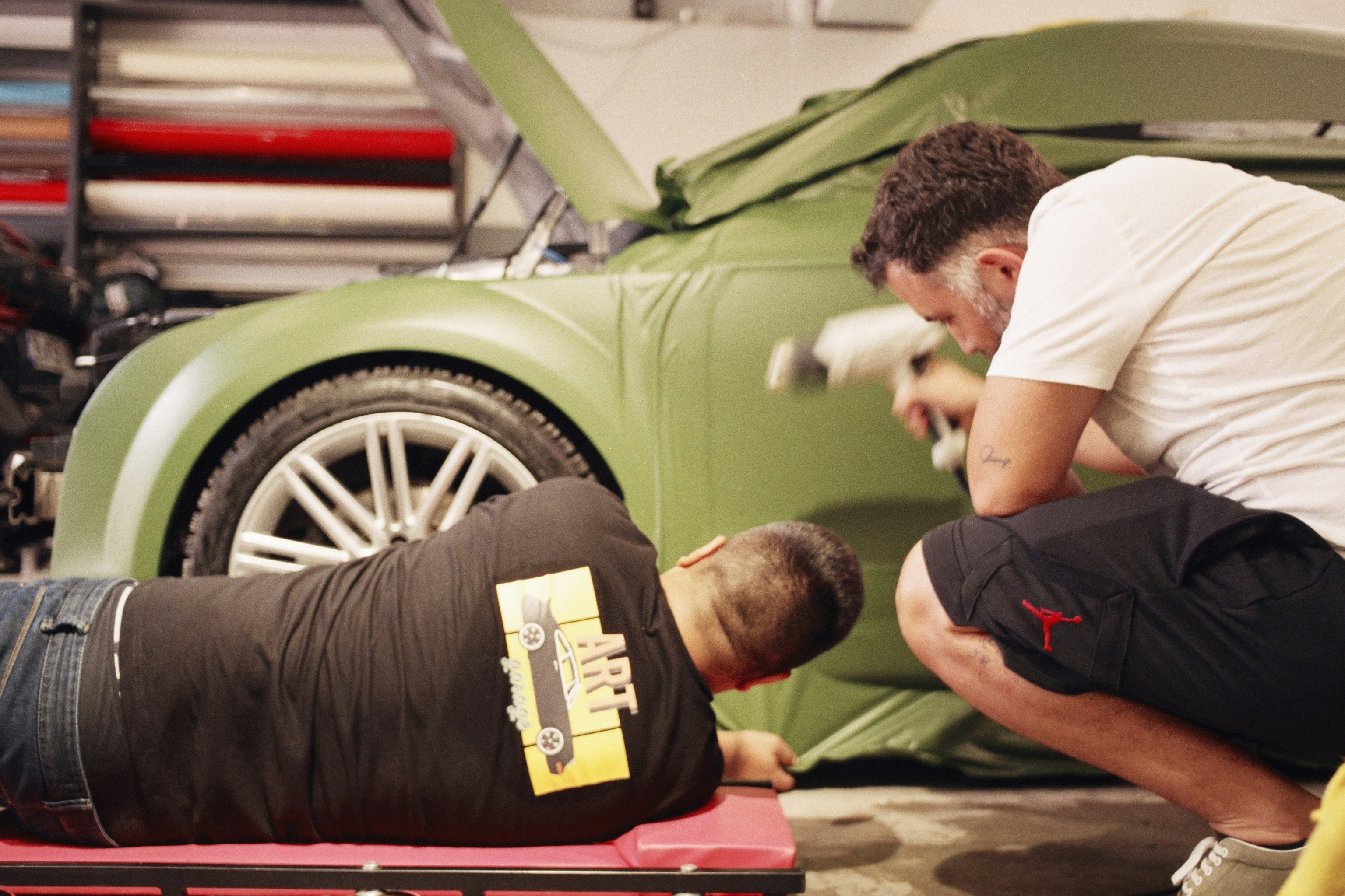 Two technicians apply olive green vinyl wrap to a car.