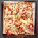 A rectangular pizza with a crispy crust topped with slices of fresh tomatoes, scattered chicken pieces, melted mozzarella cheese, and garnished with green herbs. The pizza is served on a wooden tray with a sheet of parchment paper underneath.