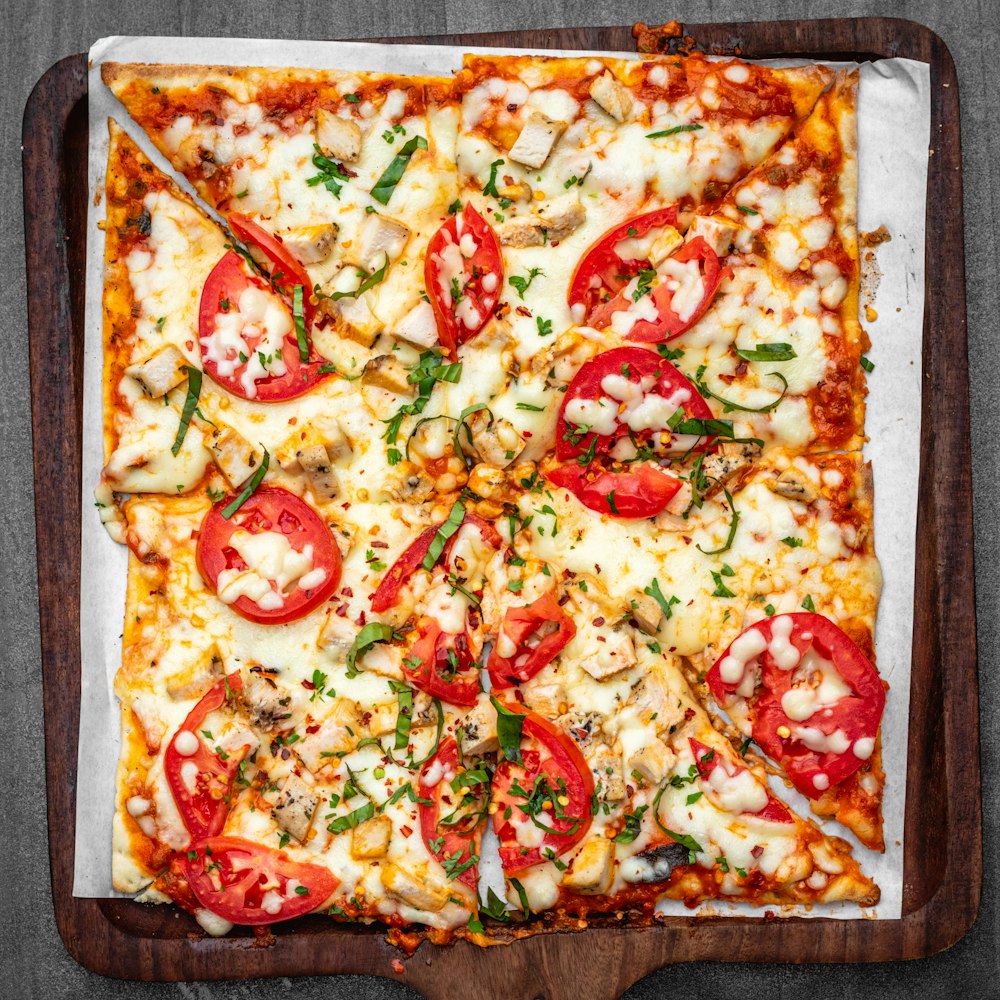 a square pizza with tomatoes and cheese on a wooden tray
