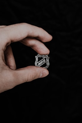 A hand holds a small object featuring the NHL logo, set against a plain, dark background.