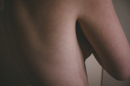 A close-up image of a human body focusing on a section of the back and side arm. The skin is pale with subtle shadows emphasizing the contours.