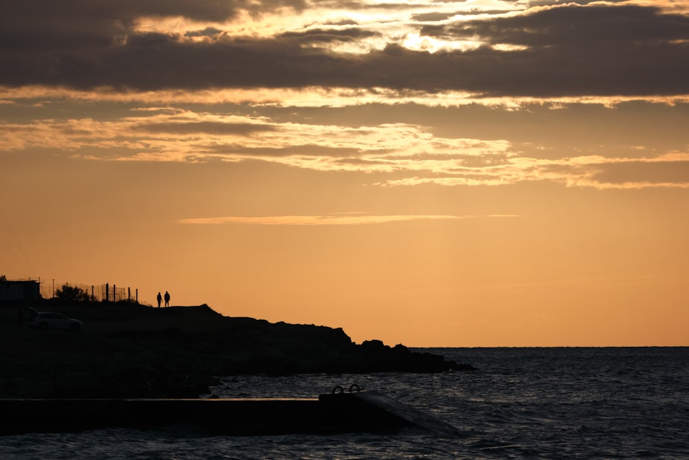 the sun is setting over the ocean with a lighthouse in the distance