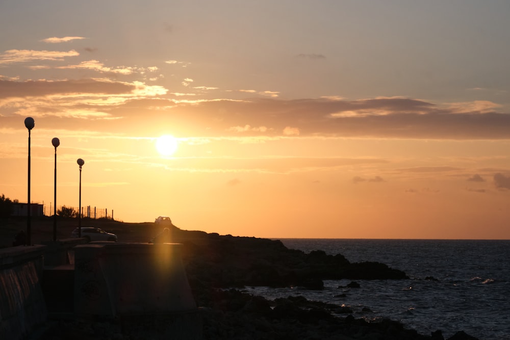 the sun is setting over the ocean near a lighthouse