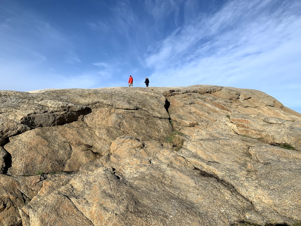 two people standing on top of a large rock