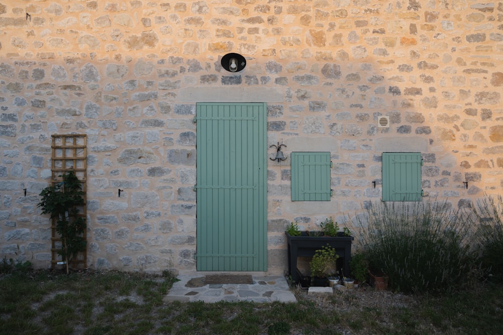 a stone building with green shutters and a potted plant