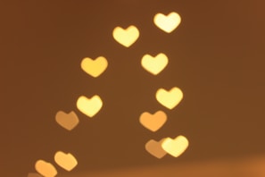 A series of heart-shaped bokeh lights are softly glowing against a warm background. The hearts are evenly spaced and vary slightly in size and brightness.