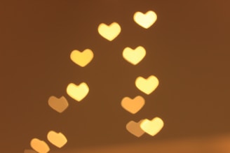 A series of heart-shaped bokeh lights are softly glowing against a warm background. The hearts are evenly spaced and vary slightly in size and brightness.