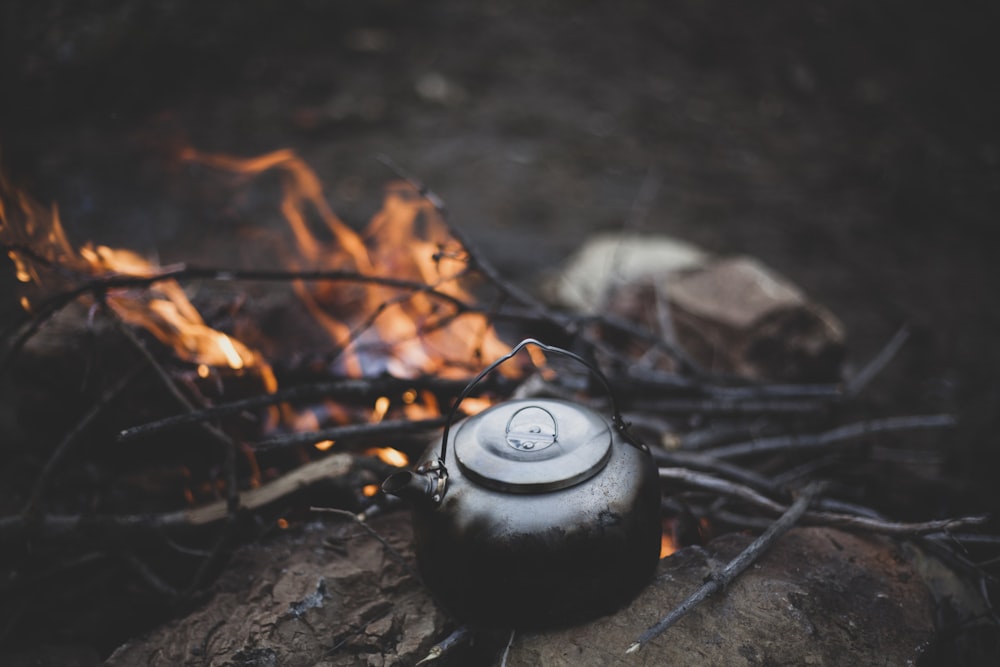 a tea pot sitting on top of a log next to a fire