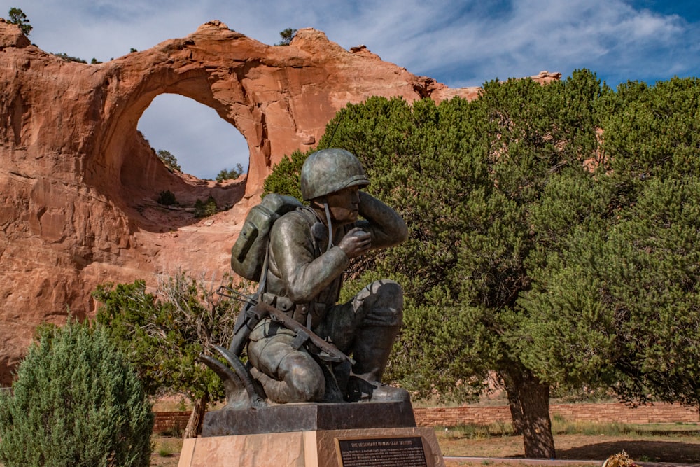 a statue of a soldier in front of a rock formation