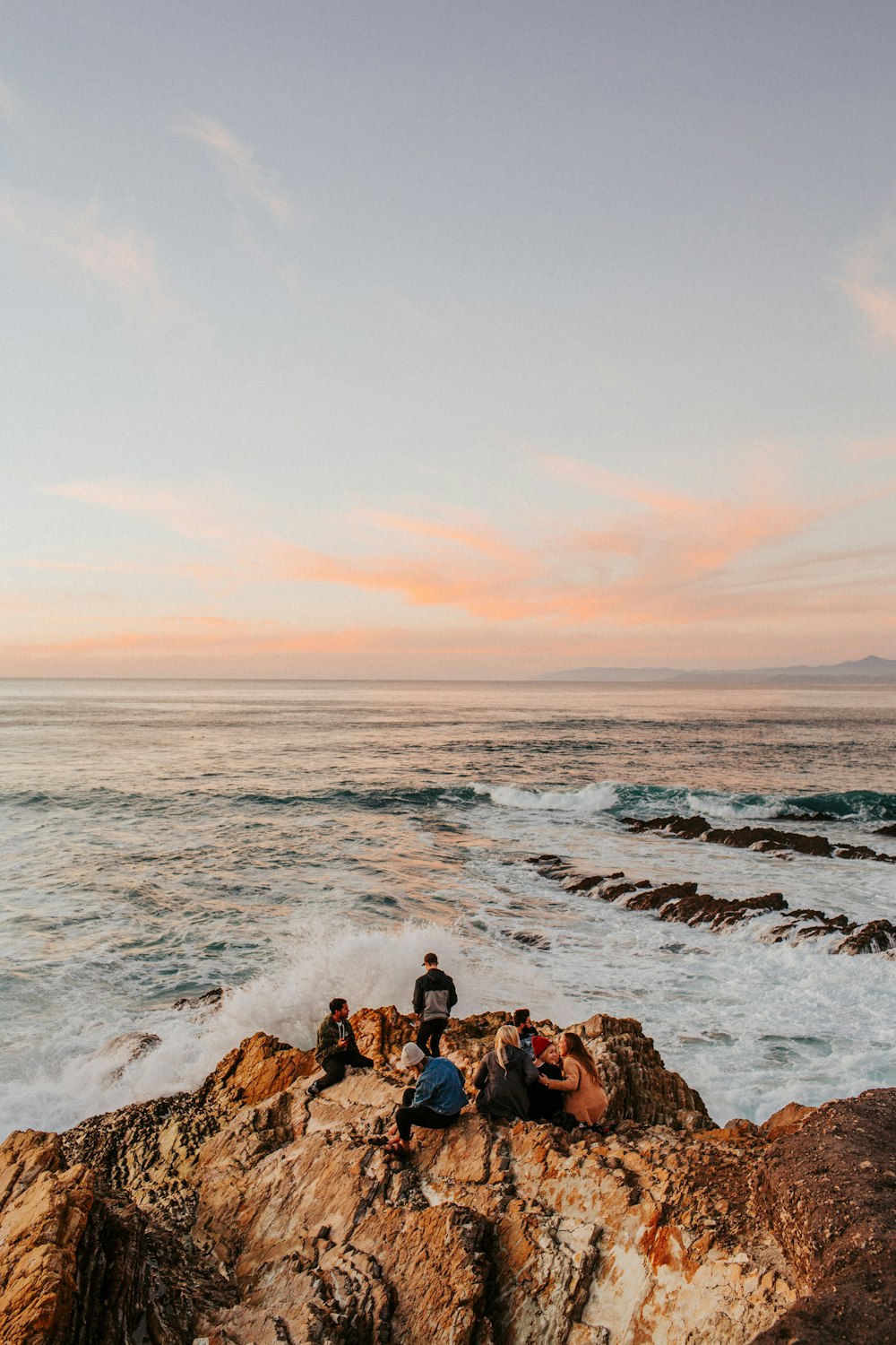 a group of people sitting on top of a rock next to the ocean