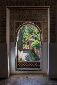 An old arched window with intricate ironwork framing a serene garden view.