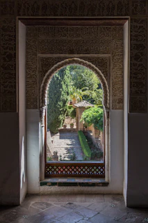 An old arched window with intricate ironwork framing a serene garden view.