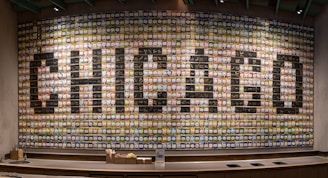 A large, colorful mural composed of numerous cups creating the word 'CHICAGO' in bold letters across a wall. The cups are arranged in a grid pattern, each with a unique design, contributing to an artistic and vibrant display.