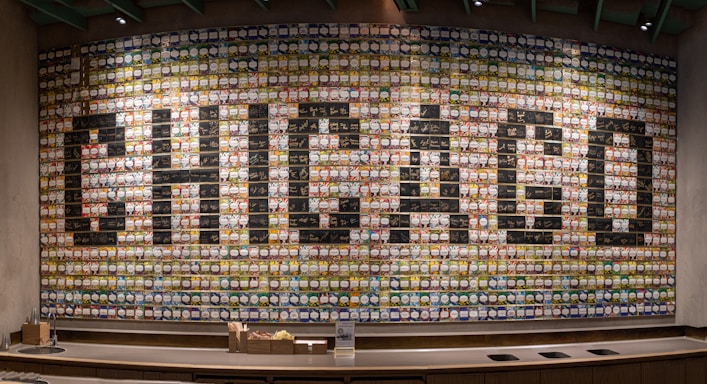 A large, colorful mural composed of numerous cups creating the word 'CHICAGO' in bold letters across a wall. The cups are arranged in a grid pattern, each with a unique design, contributing to an artistic and vibrant display.