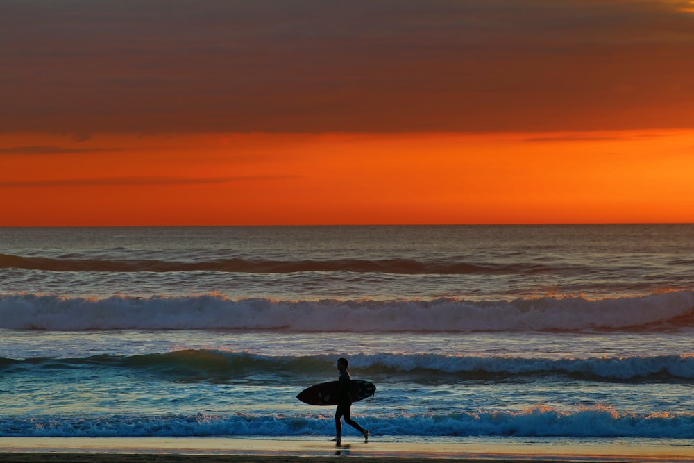 uma pessoa andando na praia com uma prancha de surf