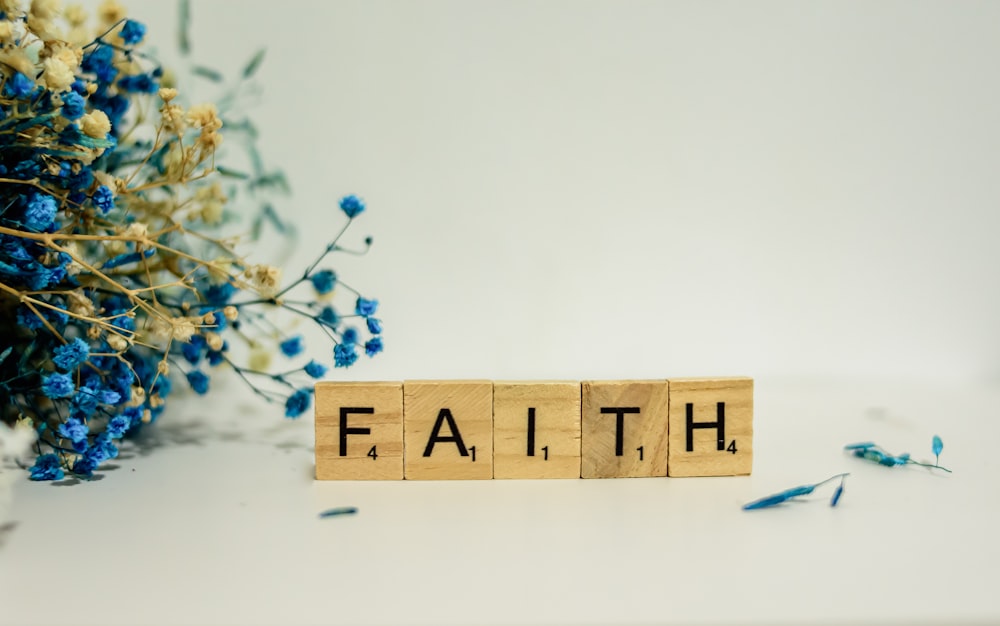 a wooden block that says faith next to blue flowers