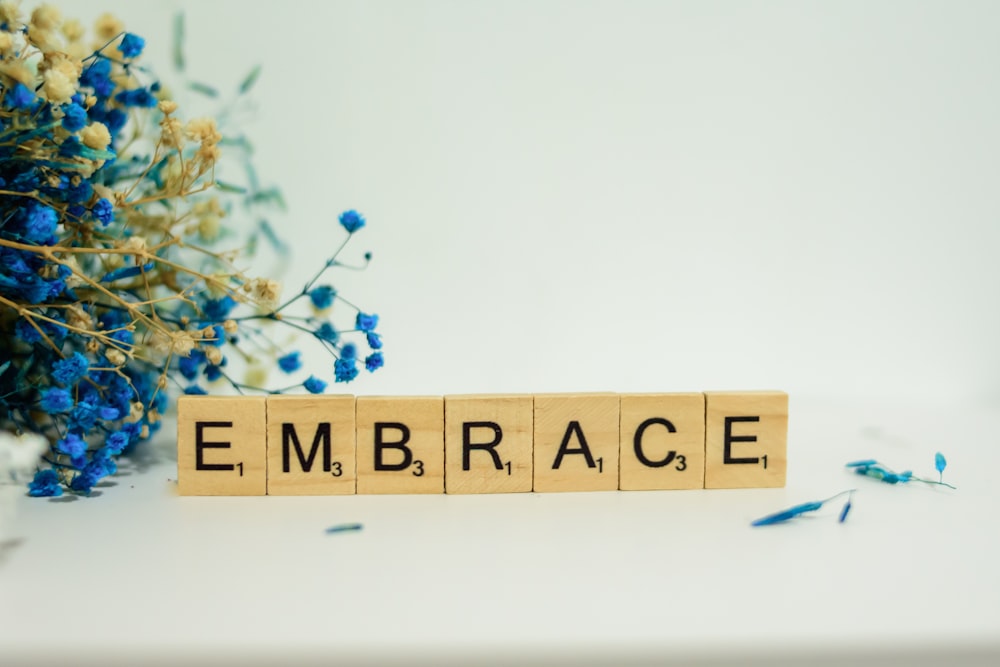 a wooden block that says embrace next to blue flowers
