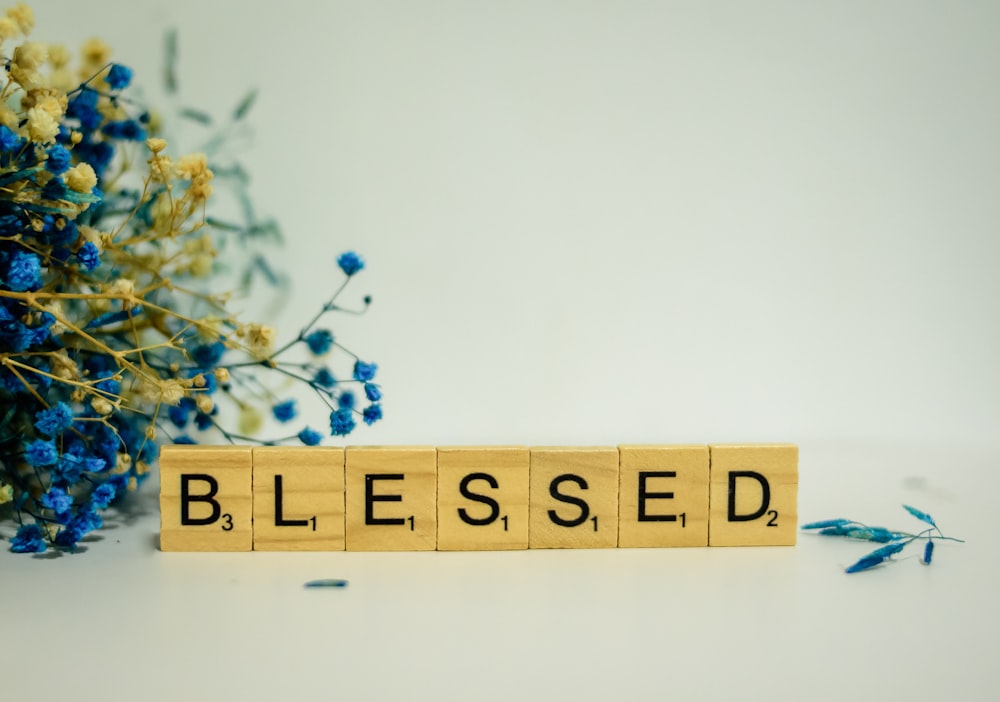 Un bloque de madera que deletrea la palabra bendición junto a un ramo de flores azules