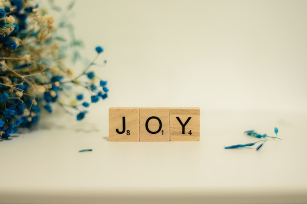 a wooden block that says joy next to a bouquet of flowers