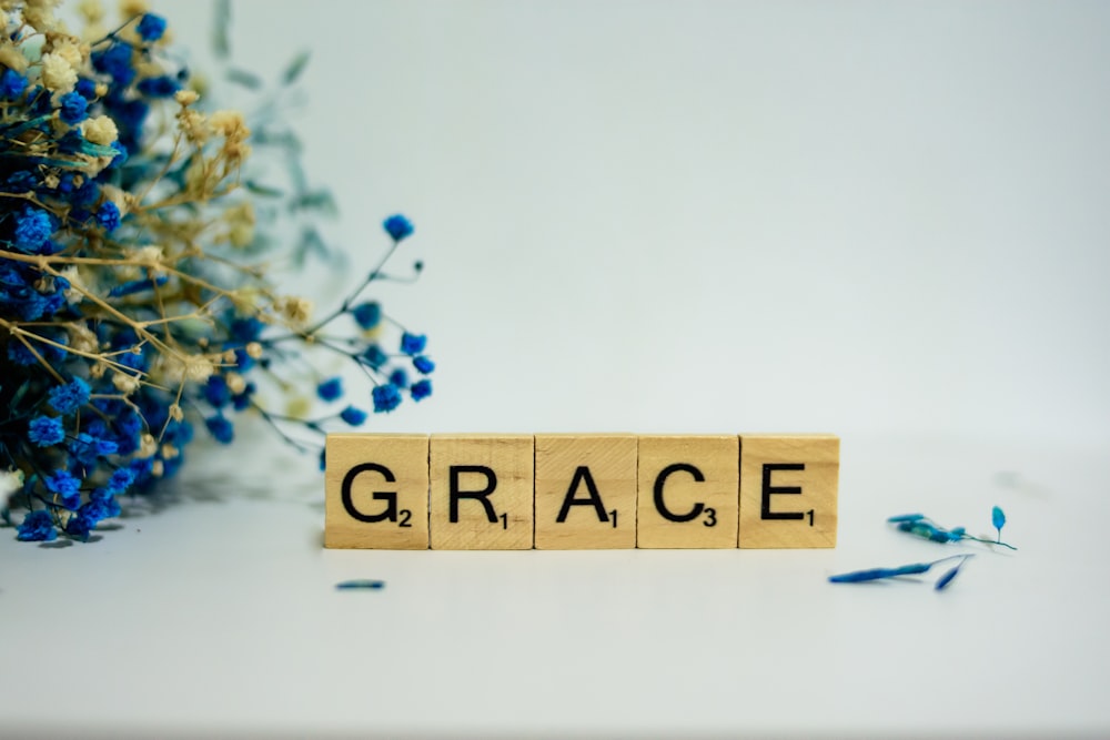 a wooden block that says grace next to a bouquet of flowers