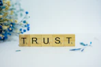 a wooden block that says trust, surrounded by blue flowers