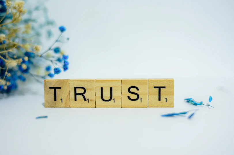 a wooden block that says trust, surrounded by blue flowers