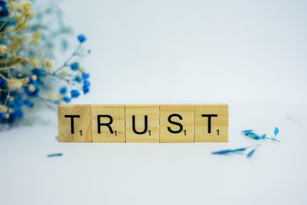 a wooden block that says trust, surrounded by blue flowers