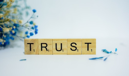 a wooden block that says trust, surrounded by blue flowers