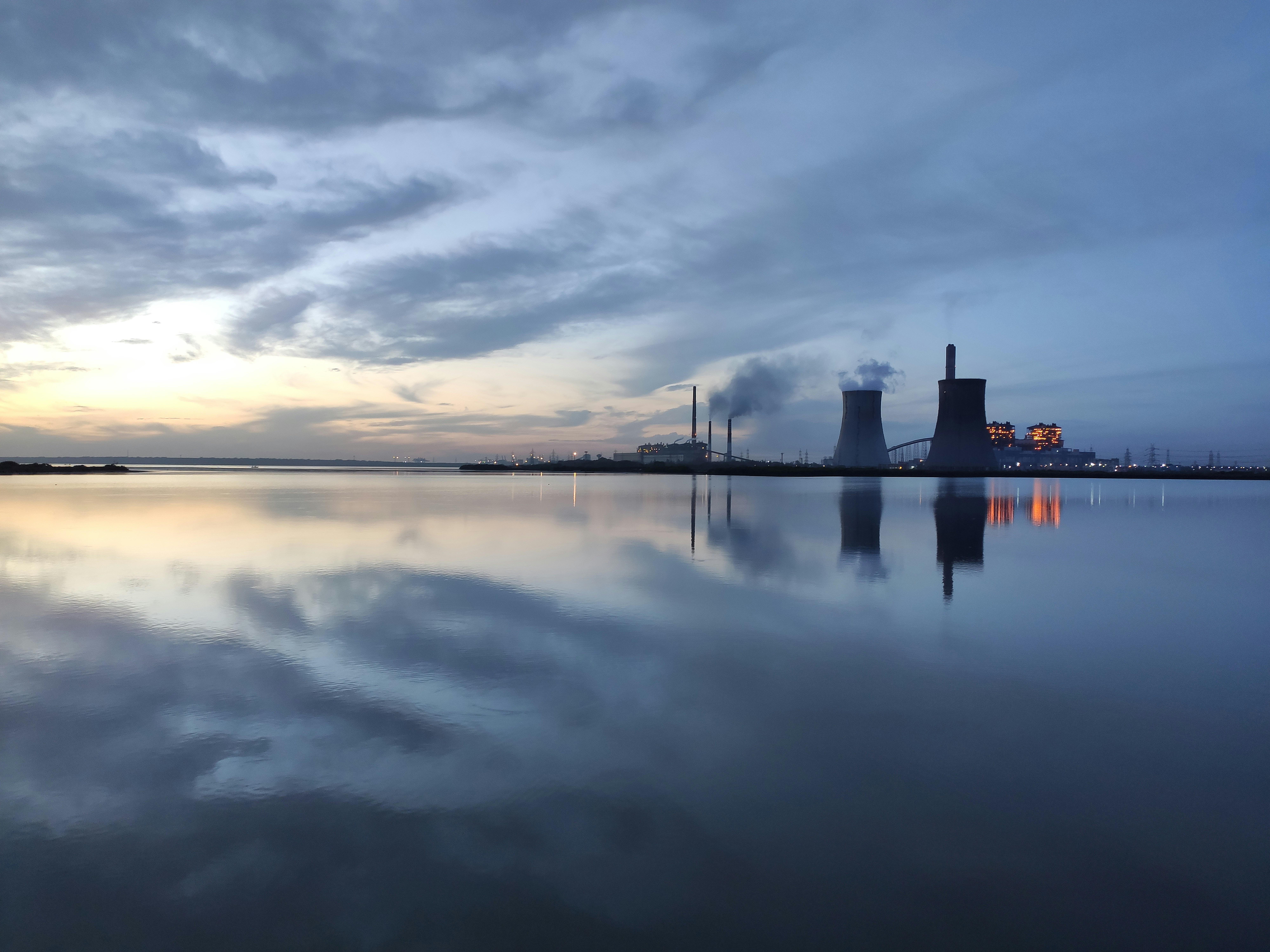 Industrial power plant cooling towers at dusk, dramatic dark sky, heavy infrastructure