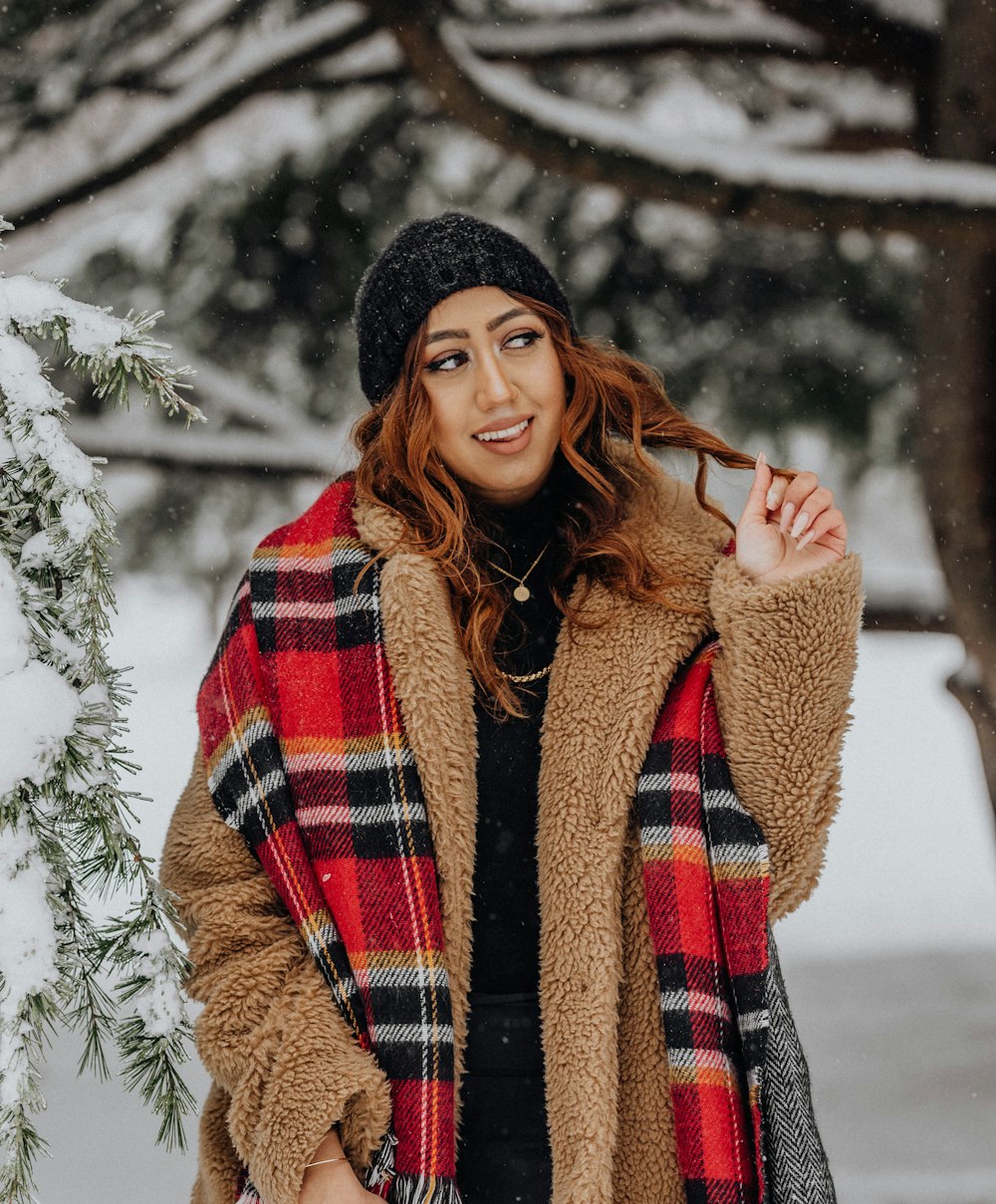 a woman standing in the snow wearing a plaid scarf