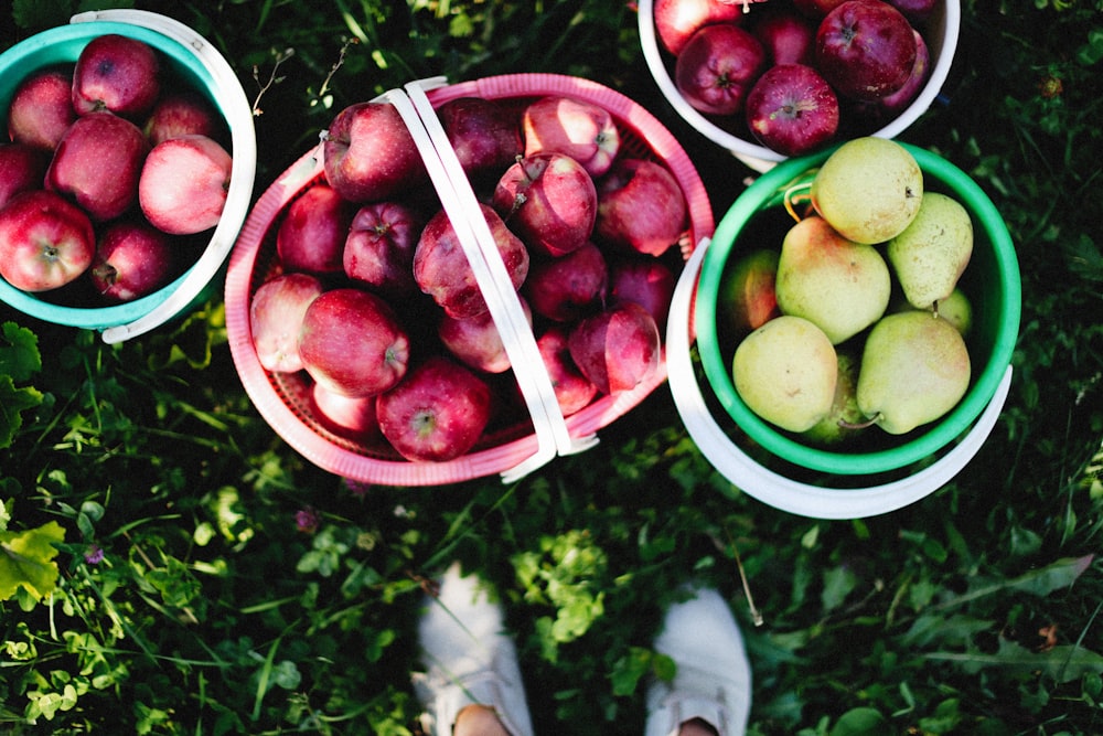 a person standing next to three buckets of apples