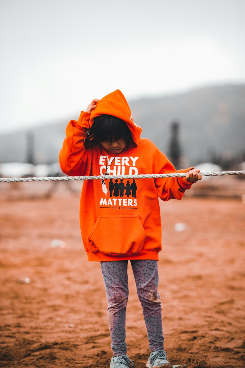 Una niña con una sudadera con capucha naranja sosteniendo una cuerda