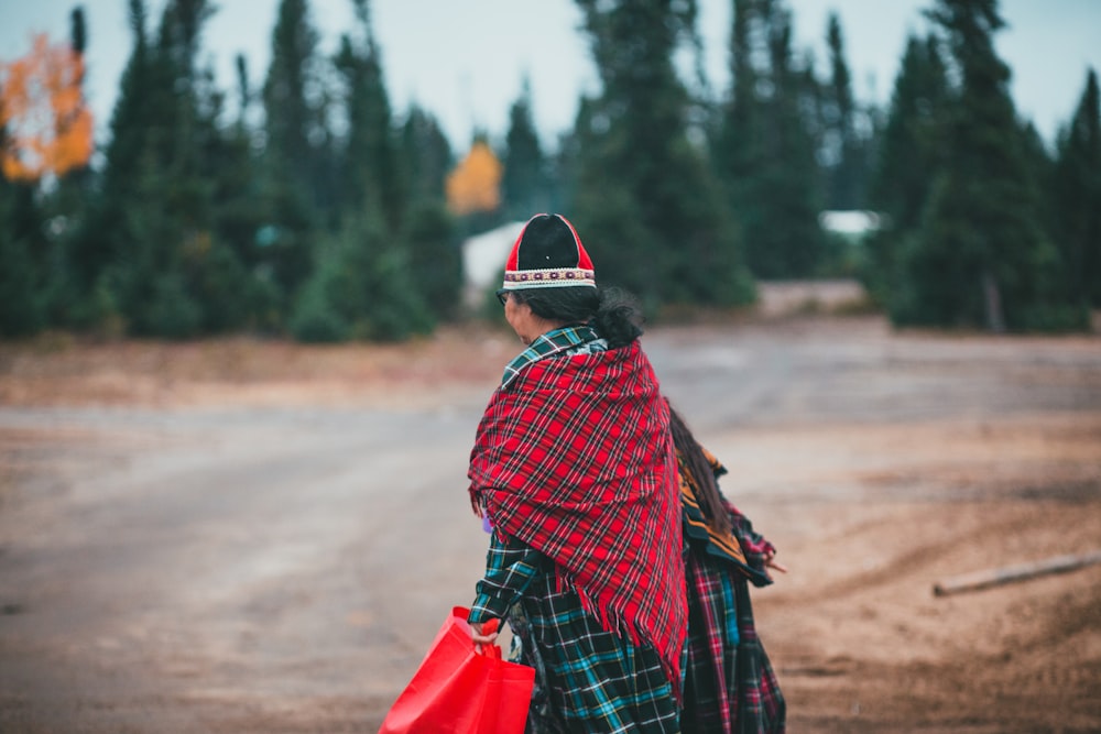 a woman walking down a dirt road carrying a red bag