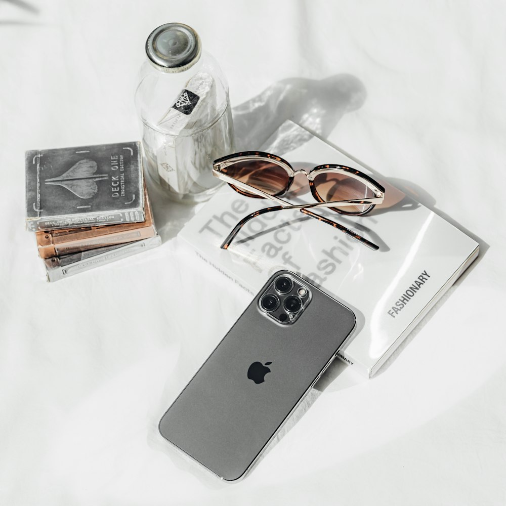 a pair of sunglasses, a book, and an iphone on a bed