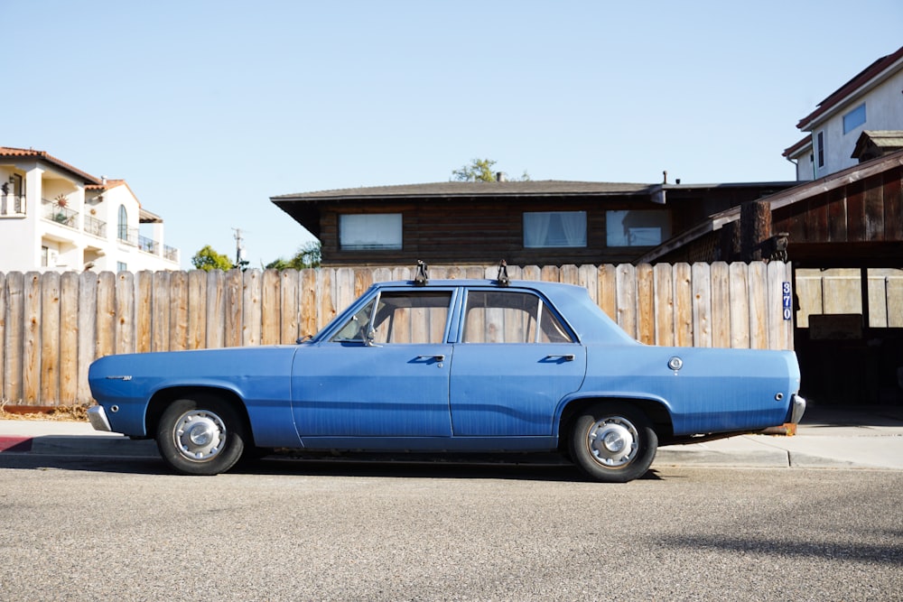 a blue car parked in front of a wooden fence