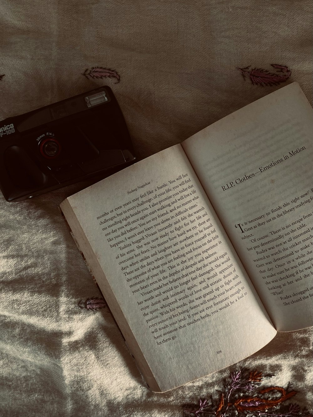 an open book sitting on top of a bed next to a camera