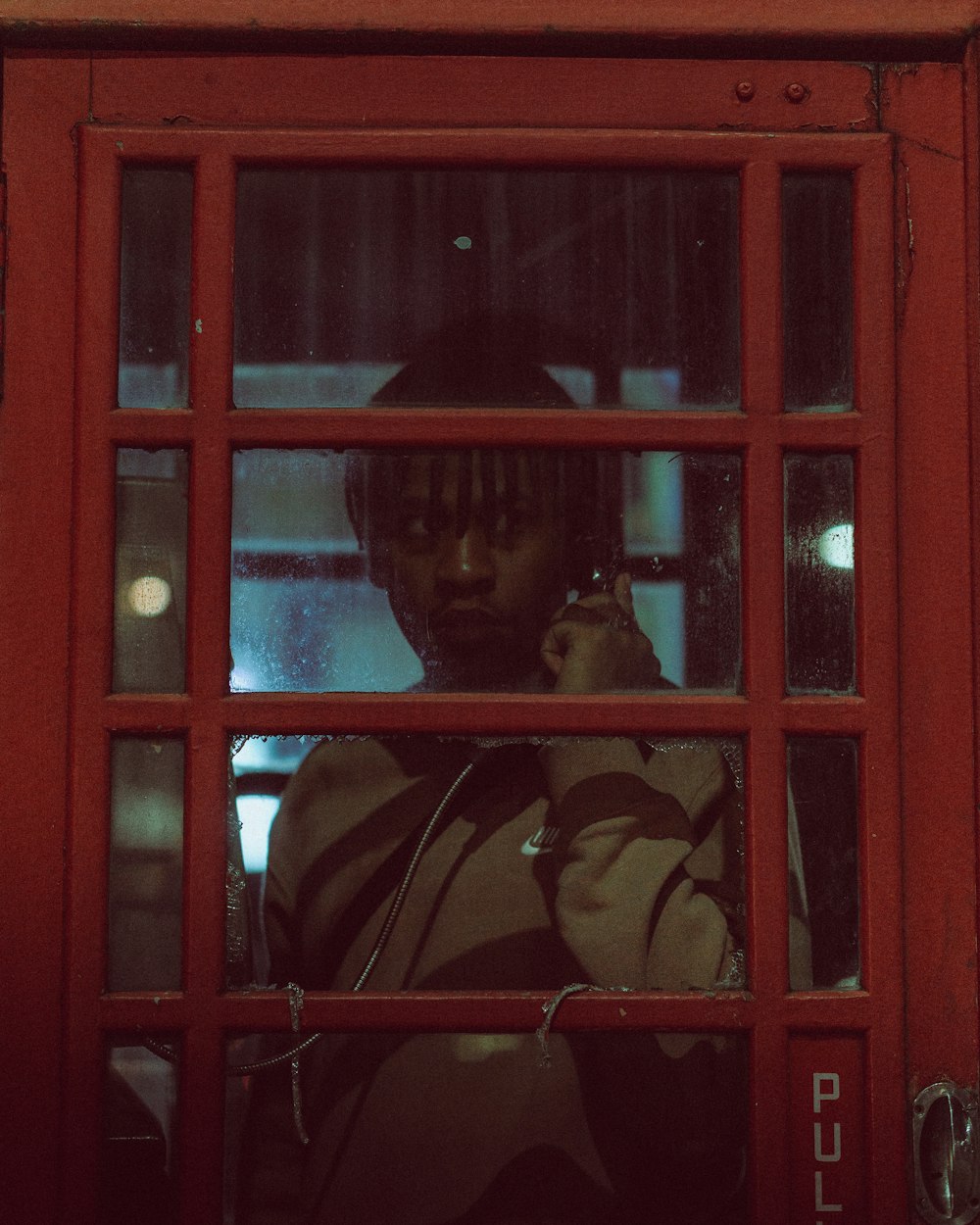 a man in a red phone booth talking on a cell phone