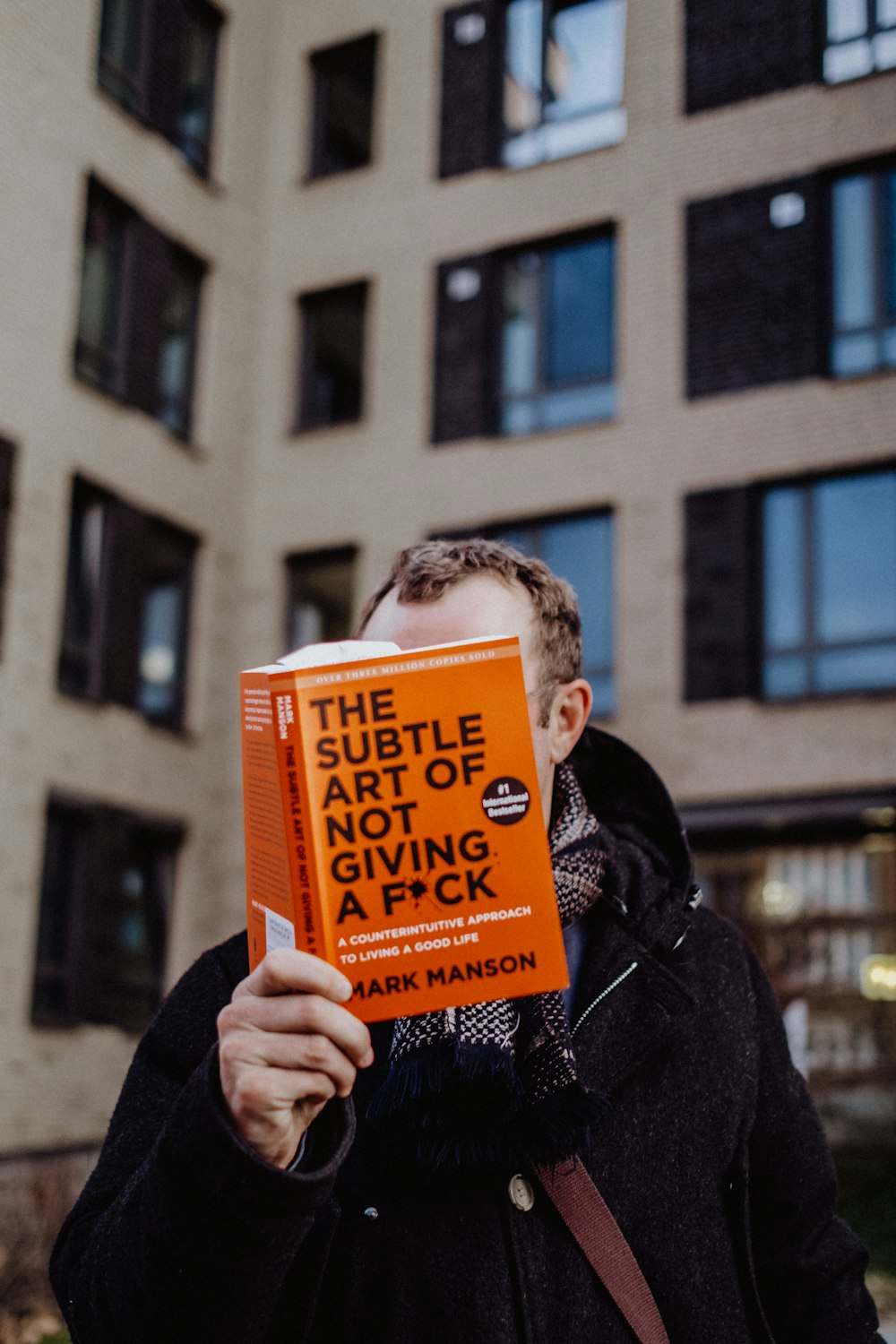 a man holding up a book in front of a building