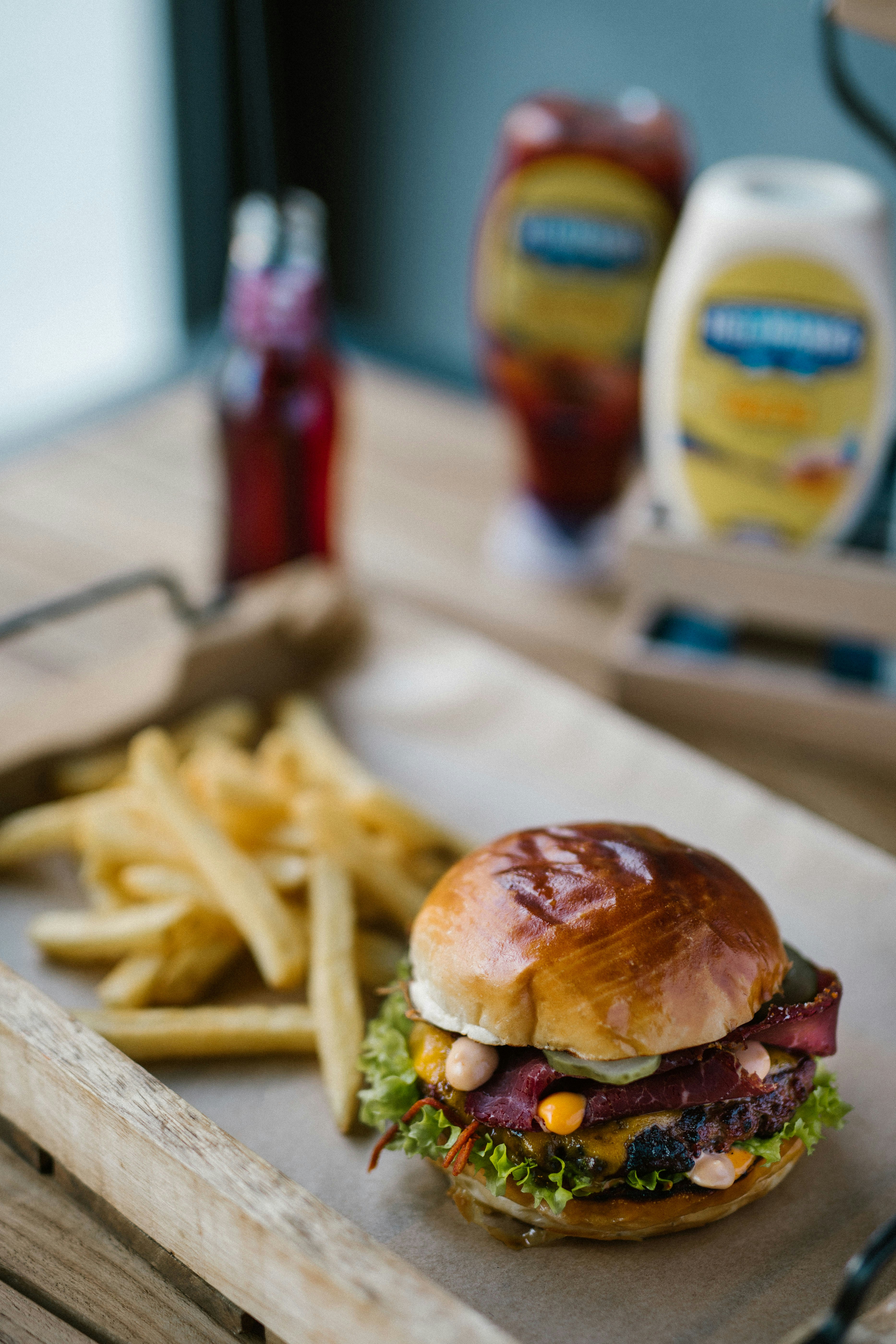 Hand reaching for burger on wooden tray with fries, warm restaurant ambiance, golden hour lighting