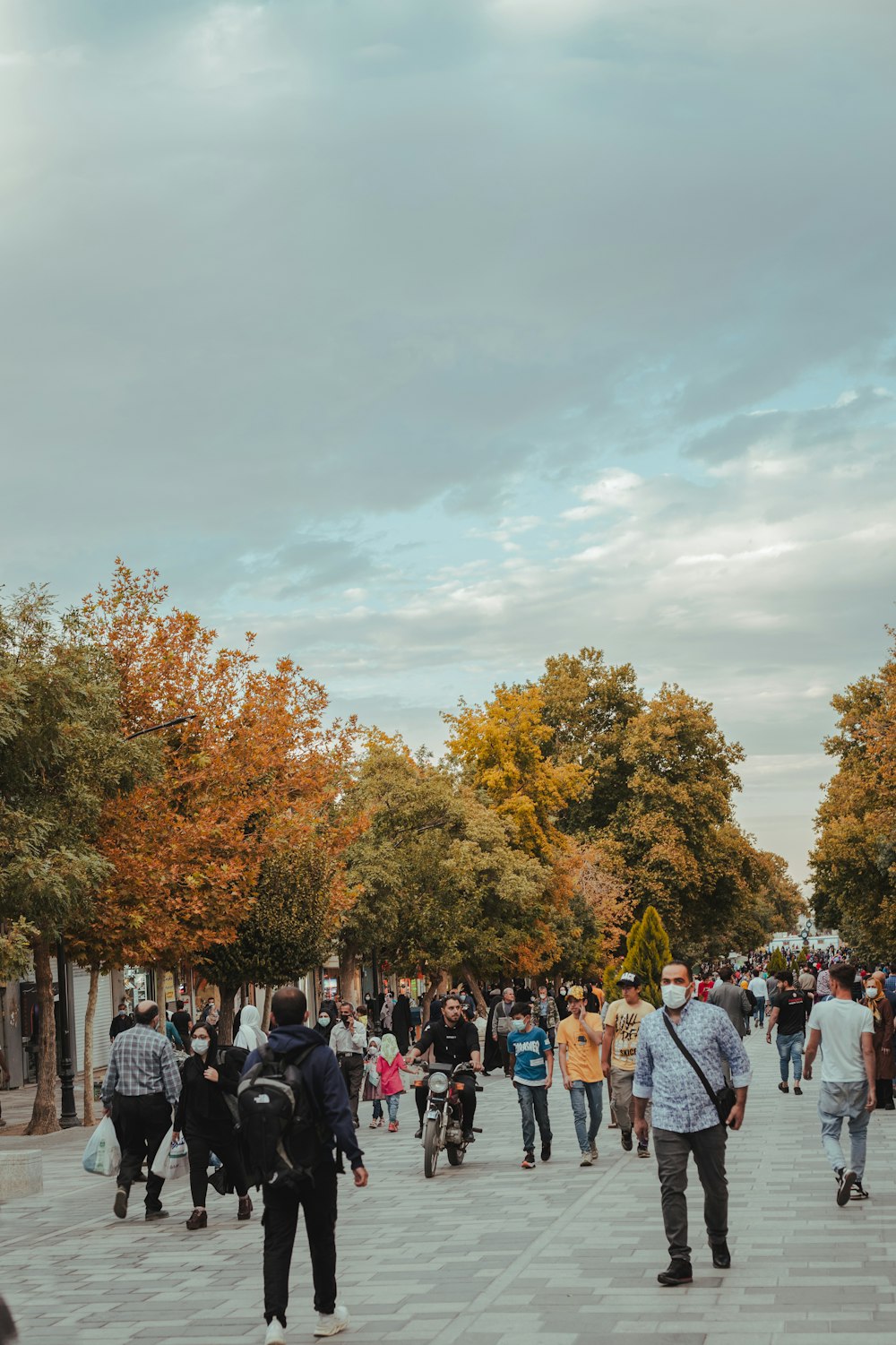 a crowd of people walking down a sidewalk next to trees