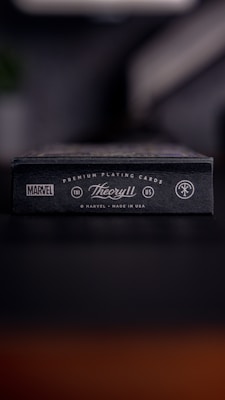 A close-up of a black box that features branding for Marvel and Theory11. The box is labeled as premium playing cards, made in the USA. It has a sleek and minimalist design with white text and logos against a dark background.