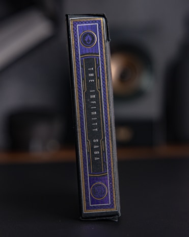 A rectangular box with elegant design elements, featuring a dark color palette with gold accents. The text 'The Infinity Saga' is prominently displayed on the side. The setting appears dark and muted, emphasizing the luxurious feel of the packaging.