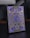 A box of playing cards adorned with intricate designs and symbols. The central focus is a large 'A' surrounded by circular emblems and geometric patterns. The design includes a combination of gold and violet hues, with various symbols often associated with superhero themes.