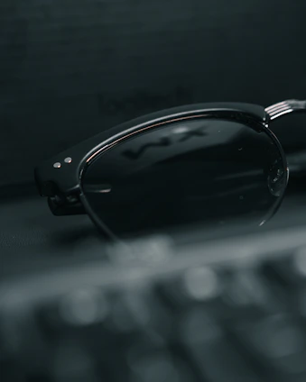 A close-up shot of sleek, futuristic smart glasses resting on a minimalist white surface with subtle digital graphics in the background.
