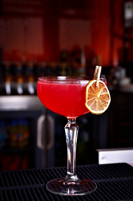 a red drink with a slice of lemon on the rim