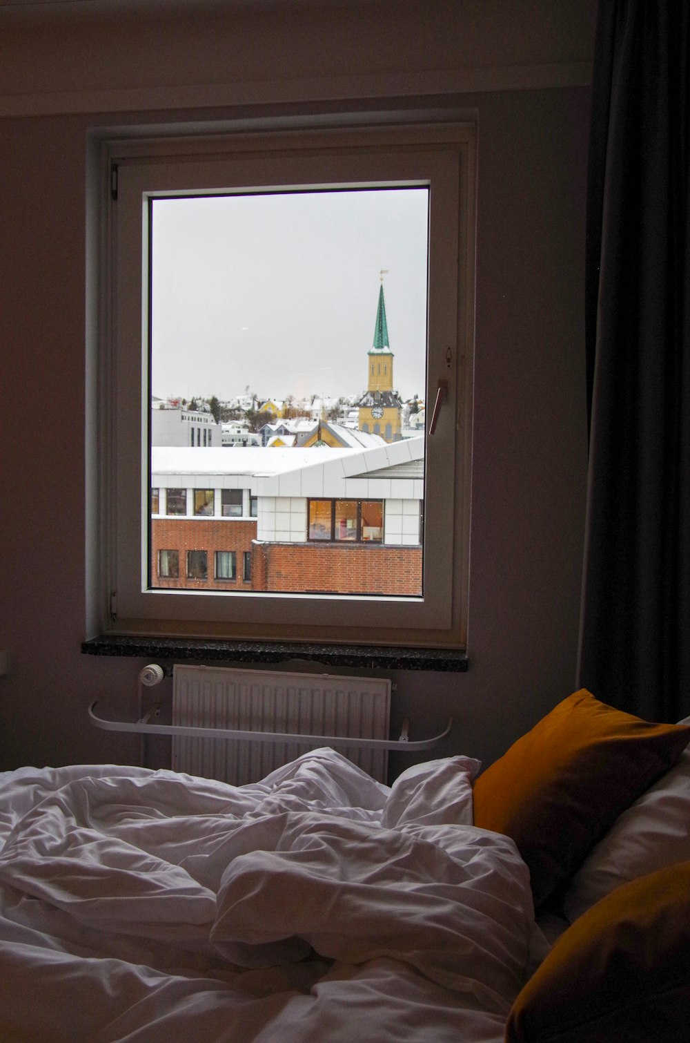a bed with a white comforter and a window with a view of a city