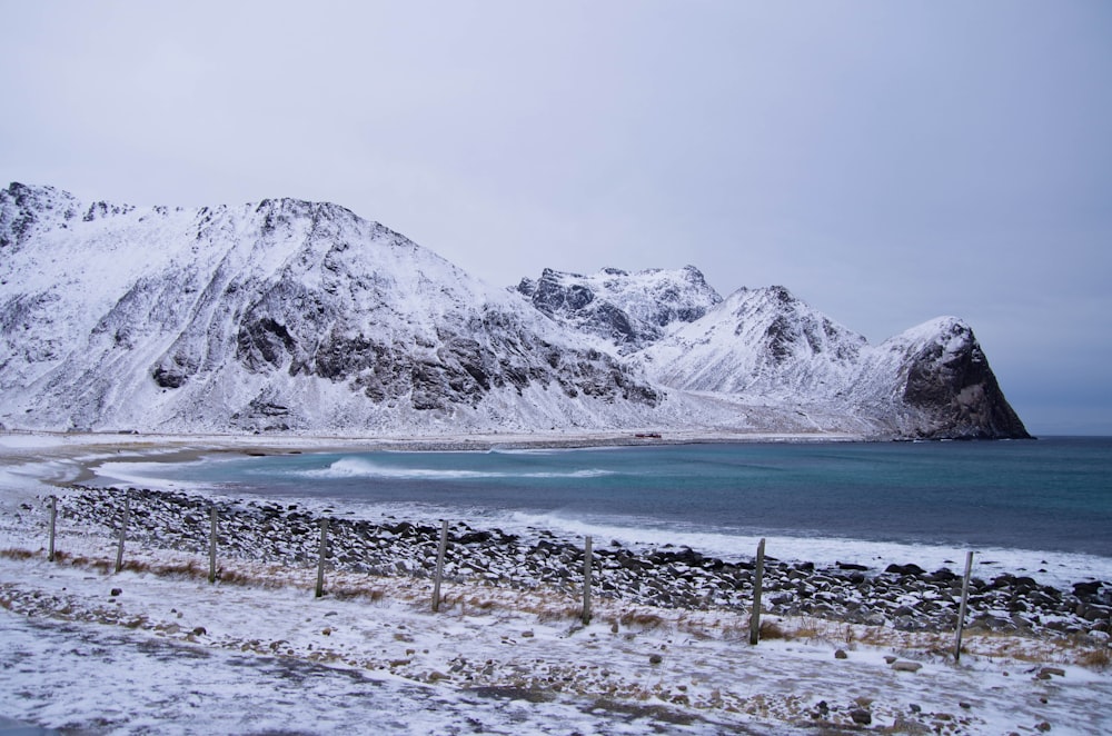 a snow covered mountain range next to a body of water