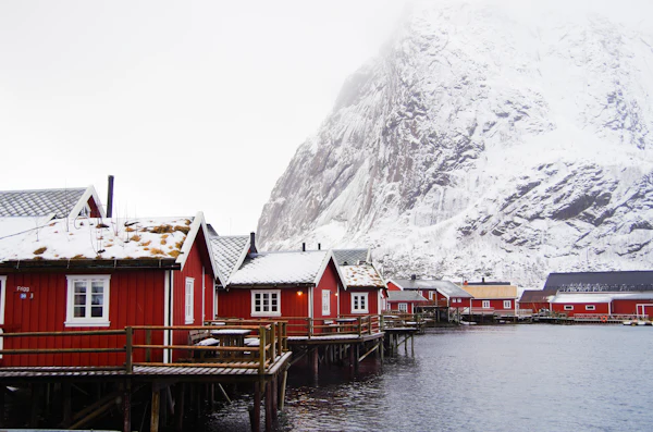 Red fishing cabins in winter beneath a snow-covered mountain at Reine in the Lofoten Islands, Norway